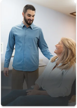 A person lies back in a dental chair, wearing safety glasses and a glowing teeth-whitening device. The setting is calm and clinical, with soft purple lighting.