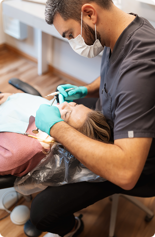 A dentist wearing gloves and a mask examines a patient's teeth in a dental chair. The setting is clinical and professional, conveying a calm, focused atmosphere.