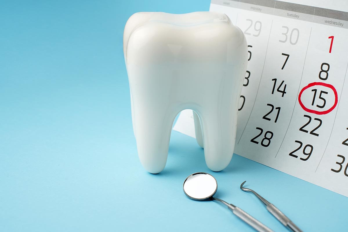 A large, white tooth model next to a calendar with the 15th circled in red. Dental tools are placed nearby on a light blue background.